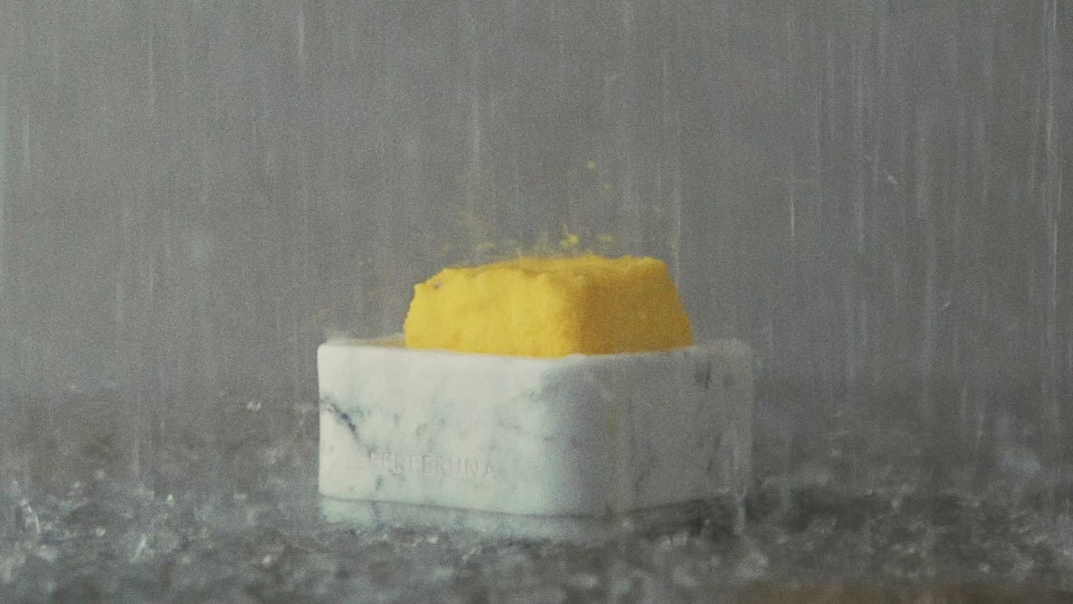 Žltá sprchová aromatická kocka v bielej kamennej miske pod prúdom vody zo sprchy